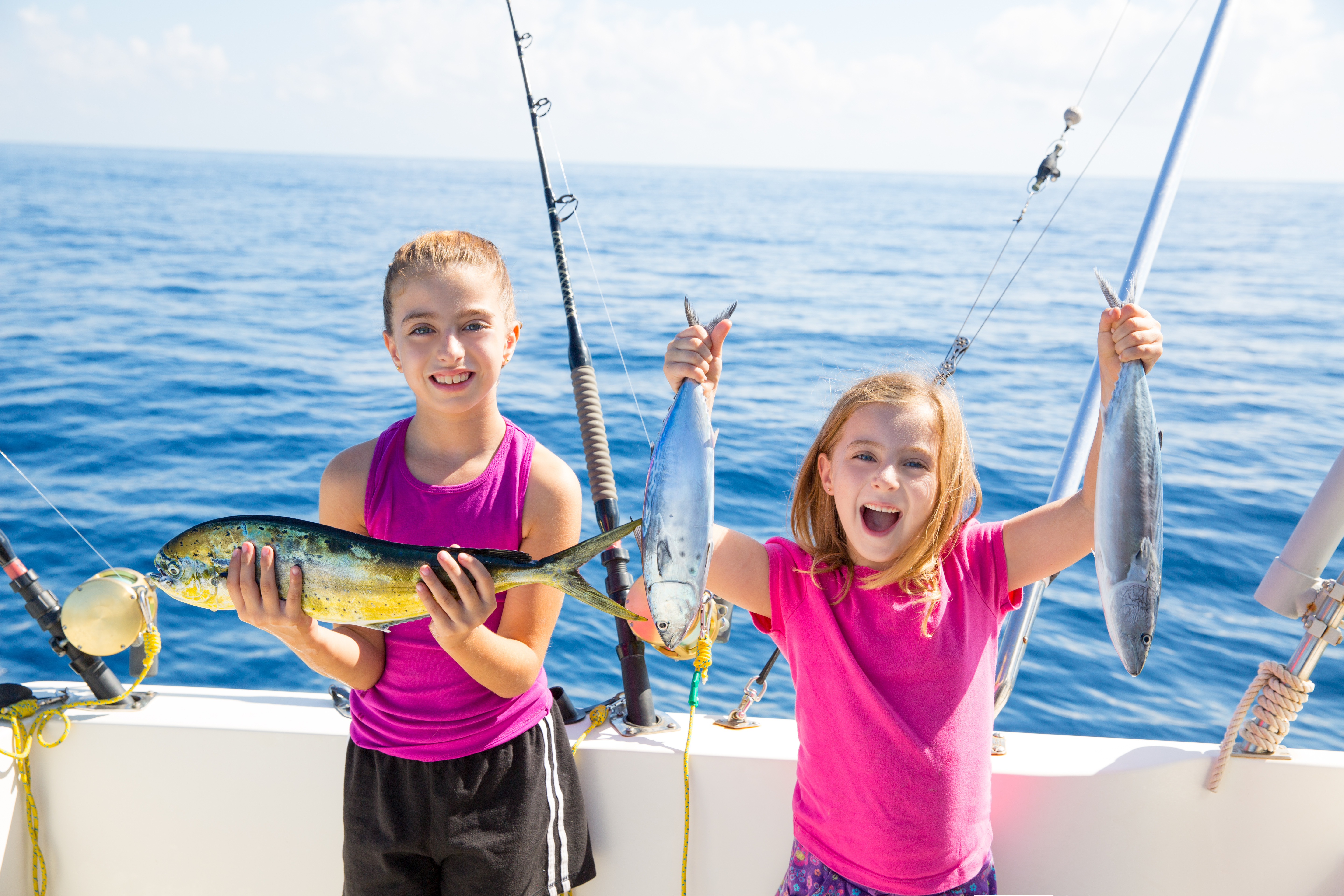 Happy tuna fisherwomen kid girls on boat with fishes trolling catch with dorado Mahi